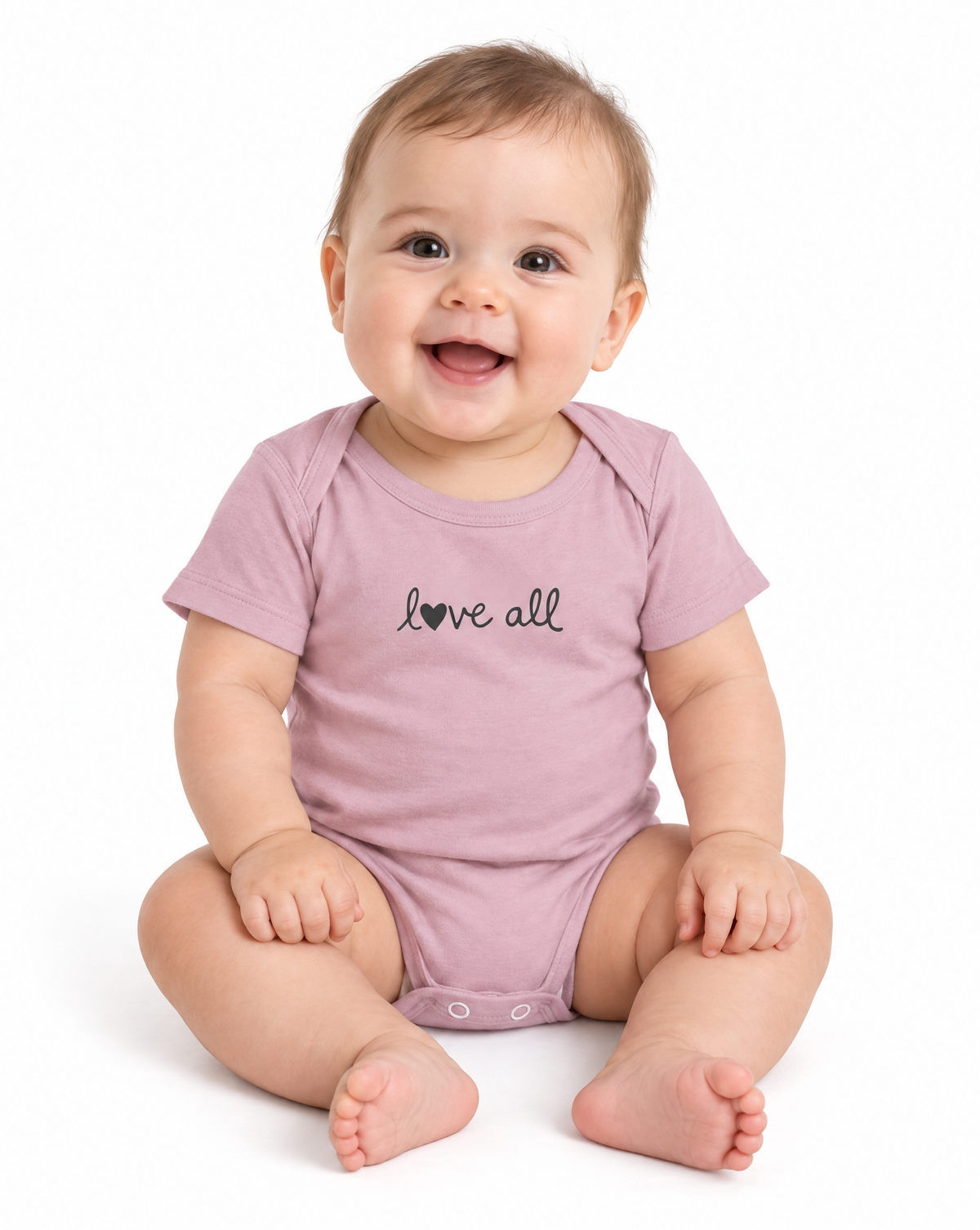 A smiling baby sitting on a white background, wearing a dusty pink short-sleeve bodysuit with the words 'love all' printed in black script across the chest.