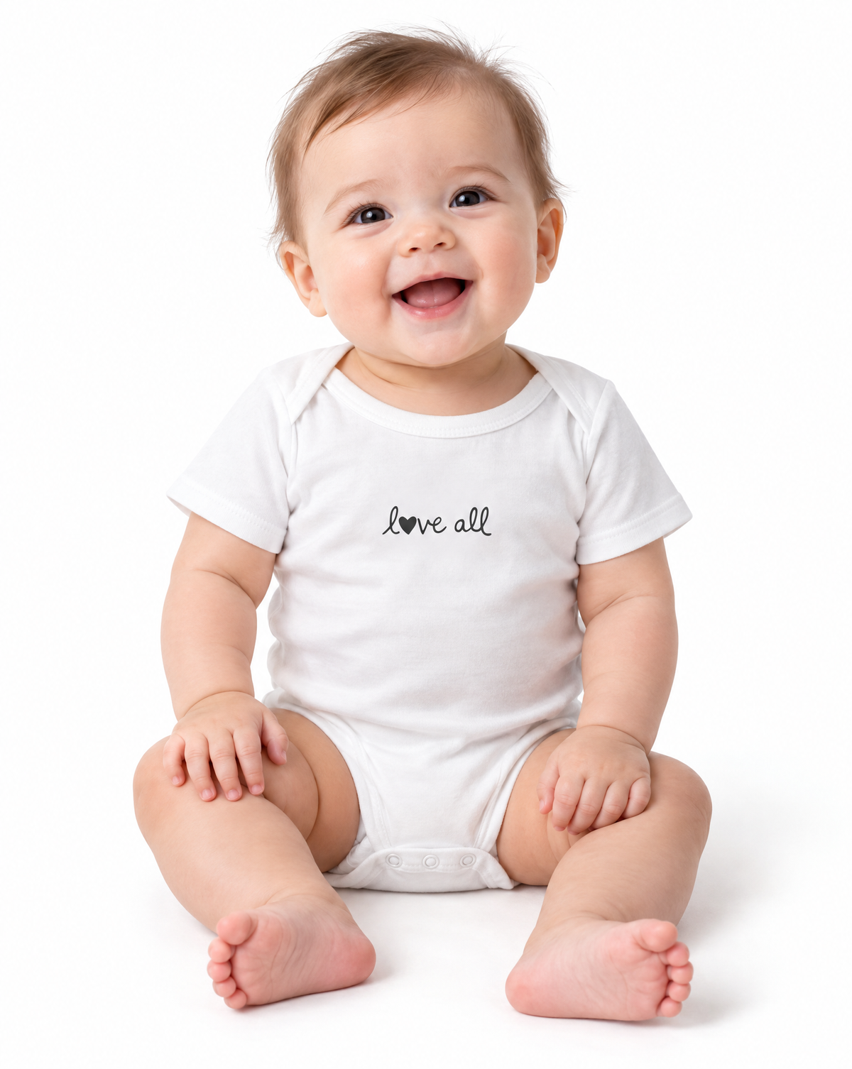 A smiling baby sitting on a white studio background, wearing a white short-sleeve bodysuit with the phrase 'love all' printed in black script across the chest.