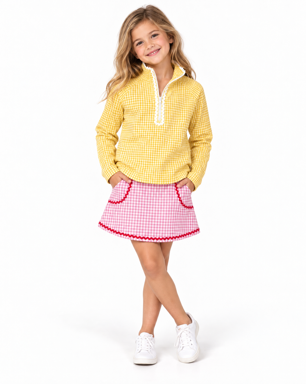 Young girl wearing a yellow and white gingham golf top with white ruffle trim and pink and white gingham golf skirt with red trim on a white studio background