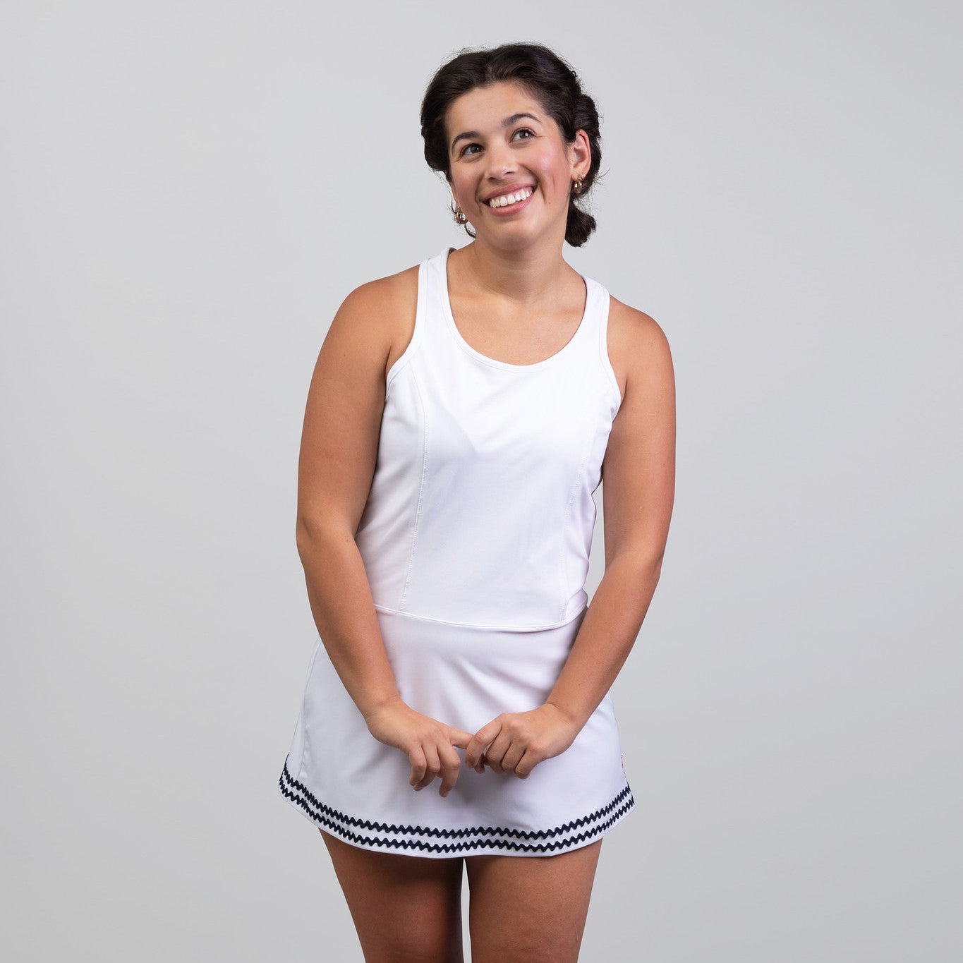 Woman wearing a white tennis dress with a skirt on a plain background