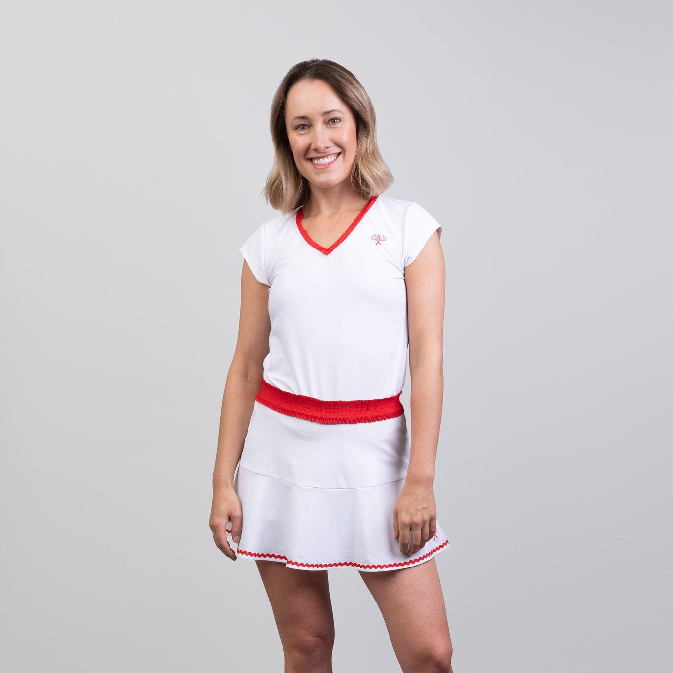 Woman wearing a white tennis skort and top with red accents on a gray background