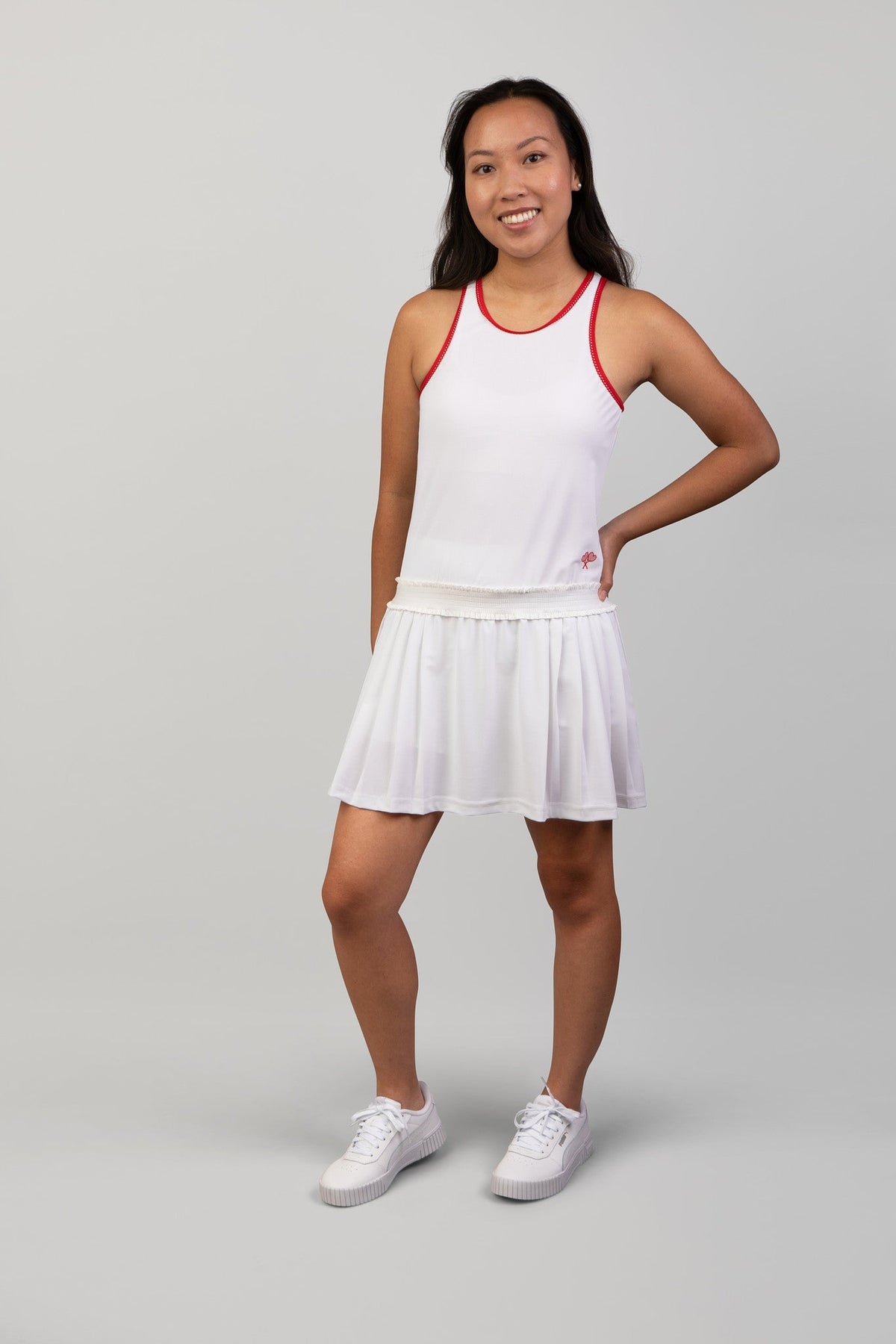 Woman wearing a white tennis outfit with red accents on a gray background