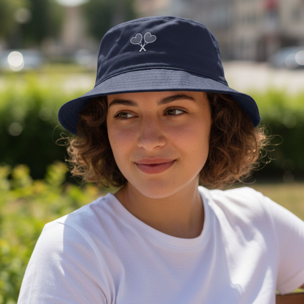 Person wearing a navy bucket hat with a logo, outdoors.