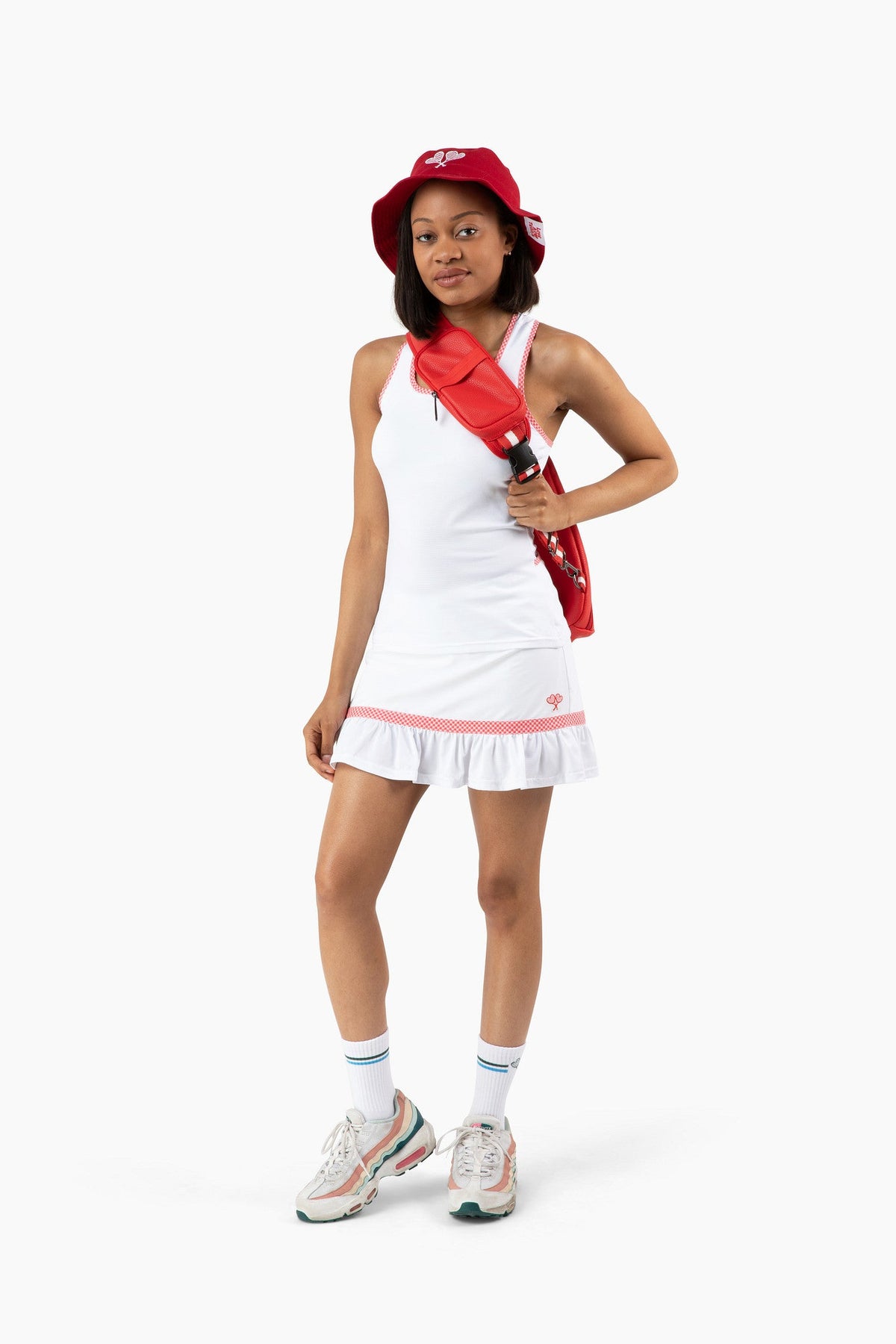 Woman wearing tennis outfit and backpack with red bucket hat and sneakers on set against a white background