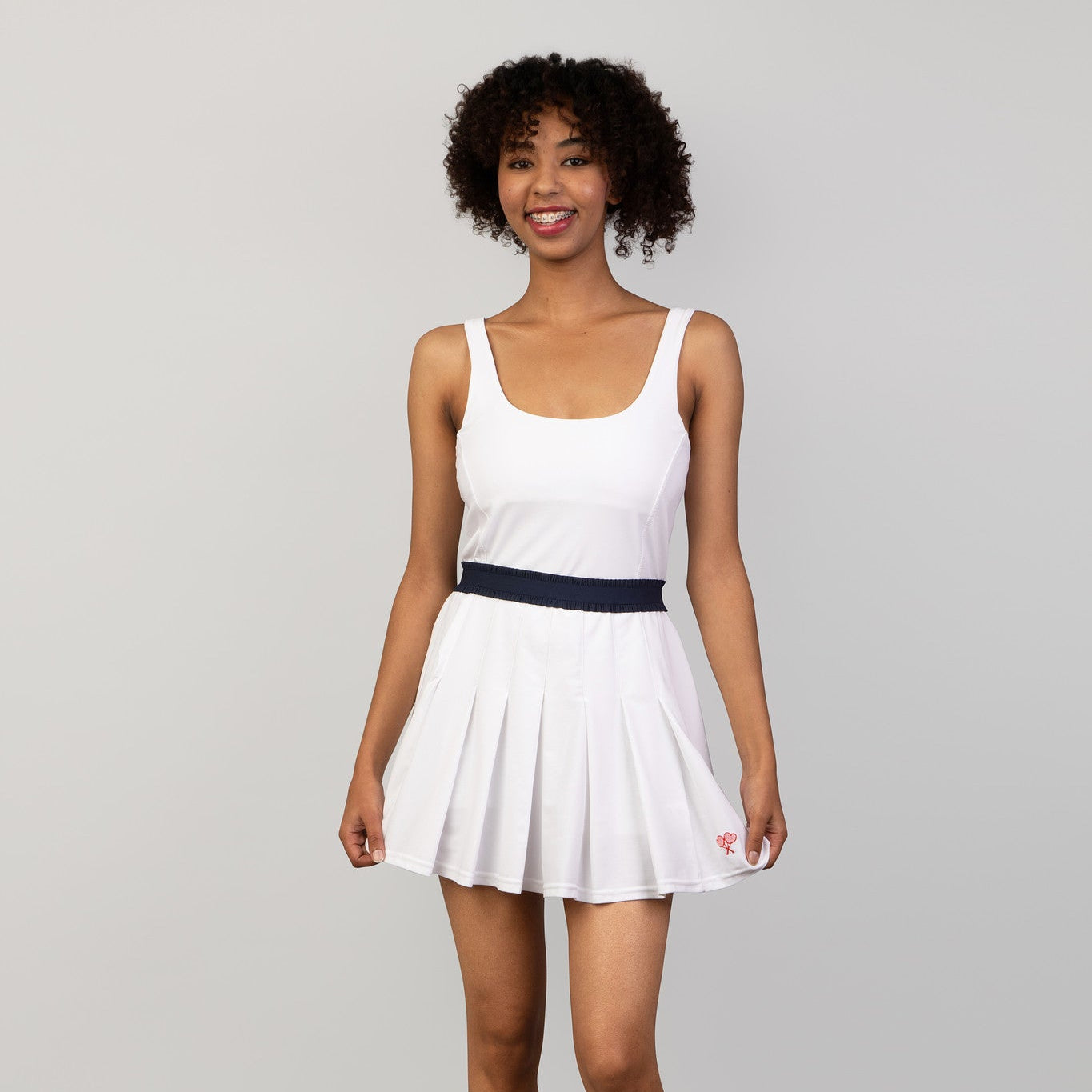 Woman wearing a white dress with a navy belt on a gray background