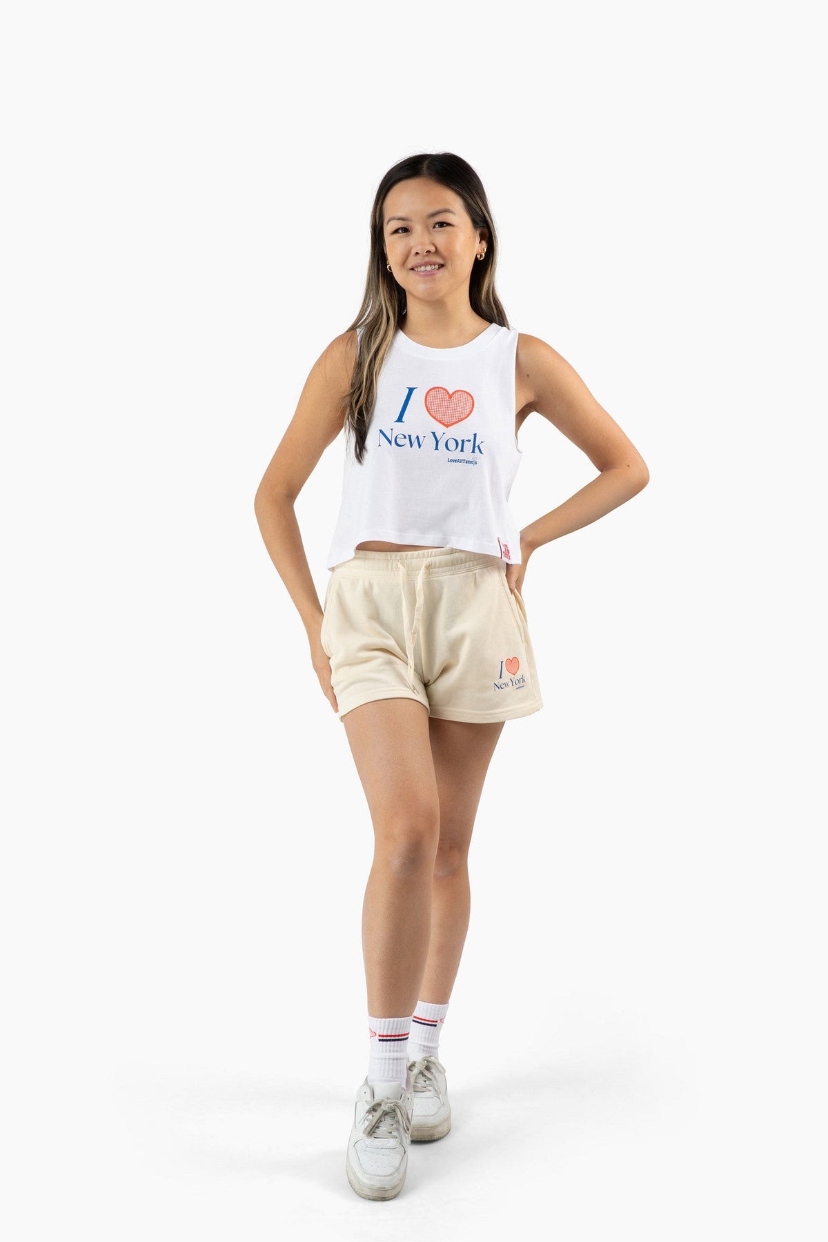 Woman wearing a white tank top and beige shorts that say "I heart New York" set against a white background