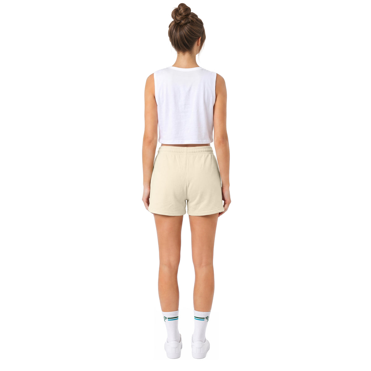 A model shown from the back wearing a white sleeveless crop top, light beige shorts, white socks, and white sneakers against a solid white background.
