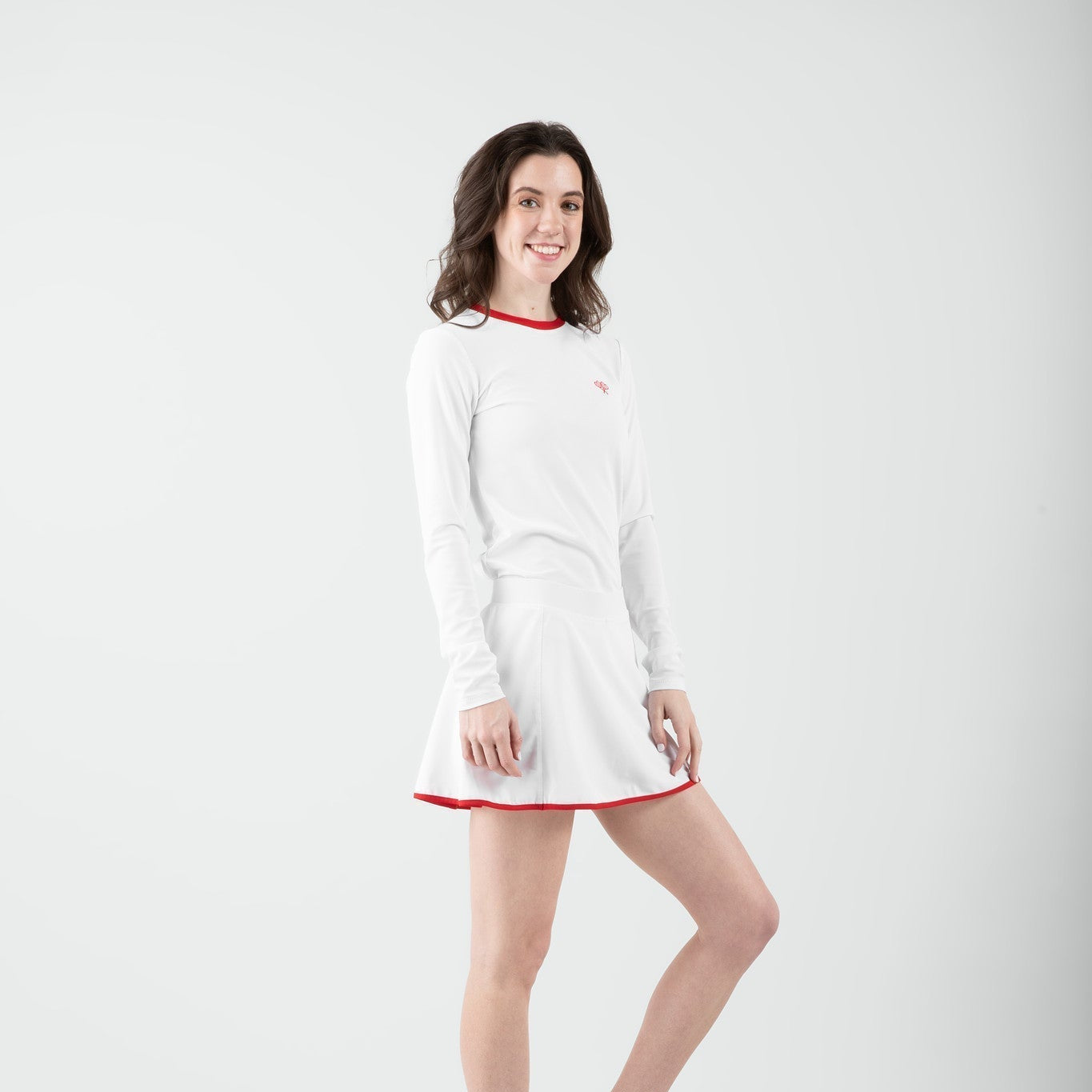 Woman wearing a white skort and top with red trim on a plain background