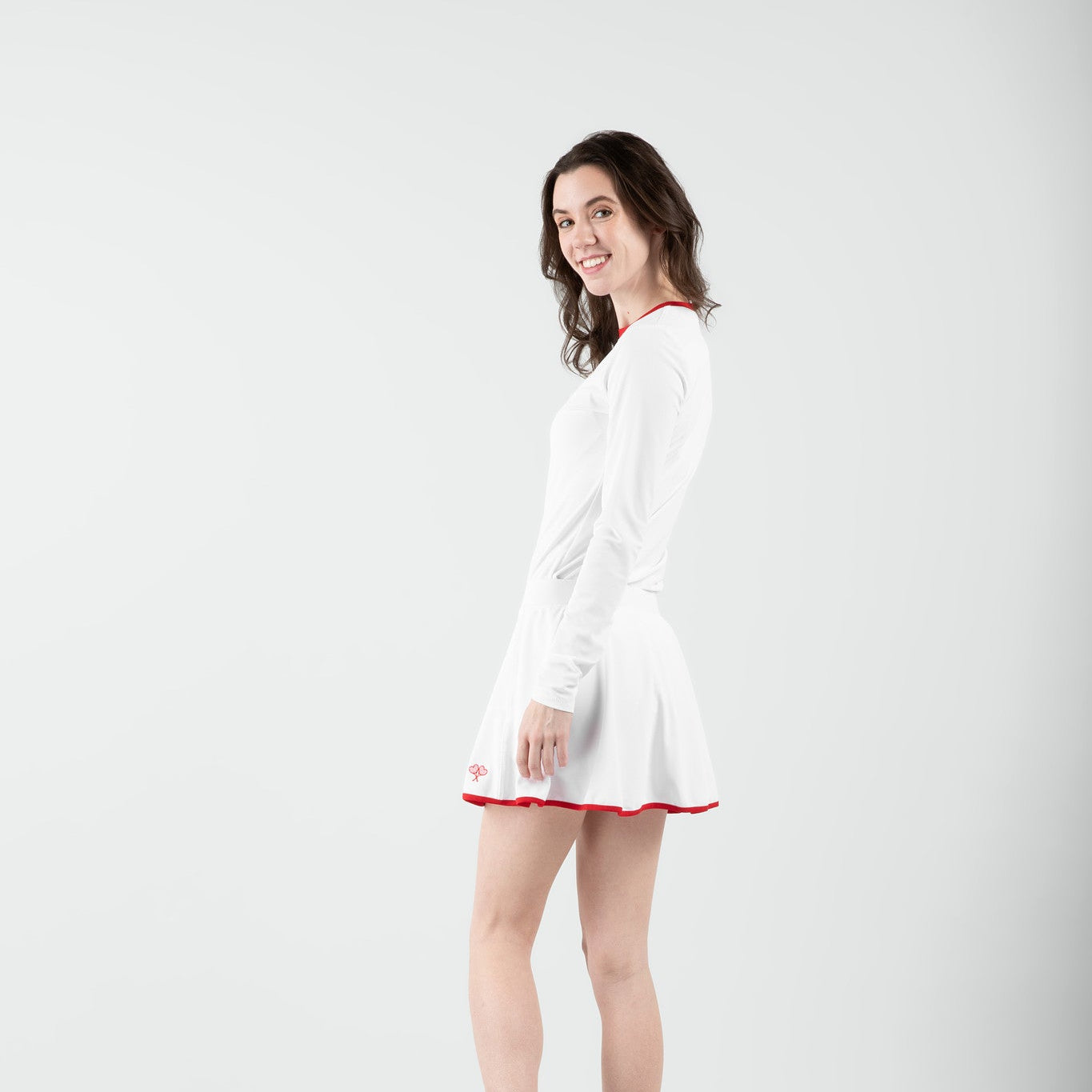 Woman wearing a white top and skort with a red trim on a plain background