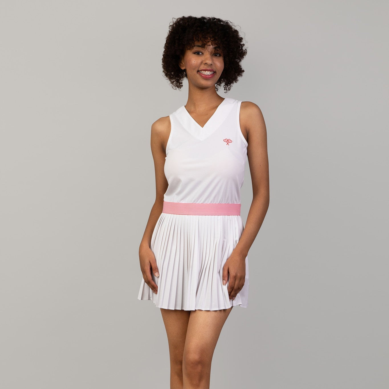 Woman wearing a white tennis dress with a pink belt on a gray background