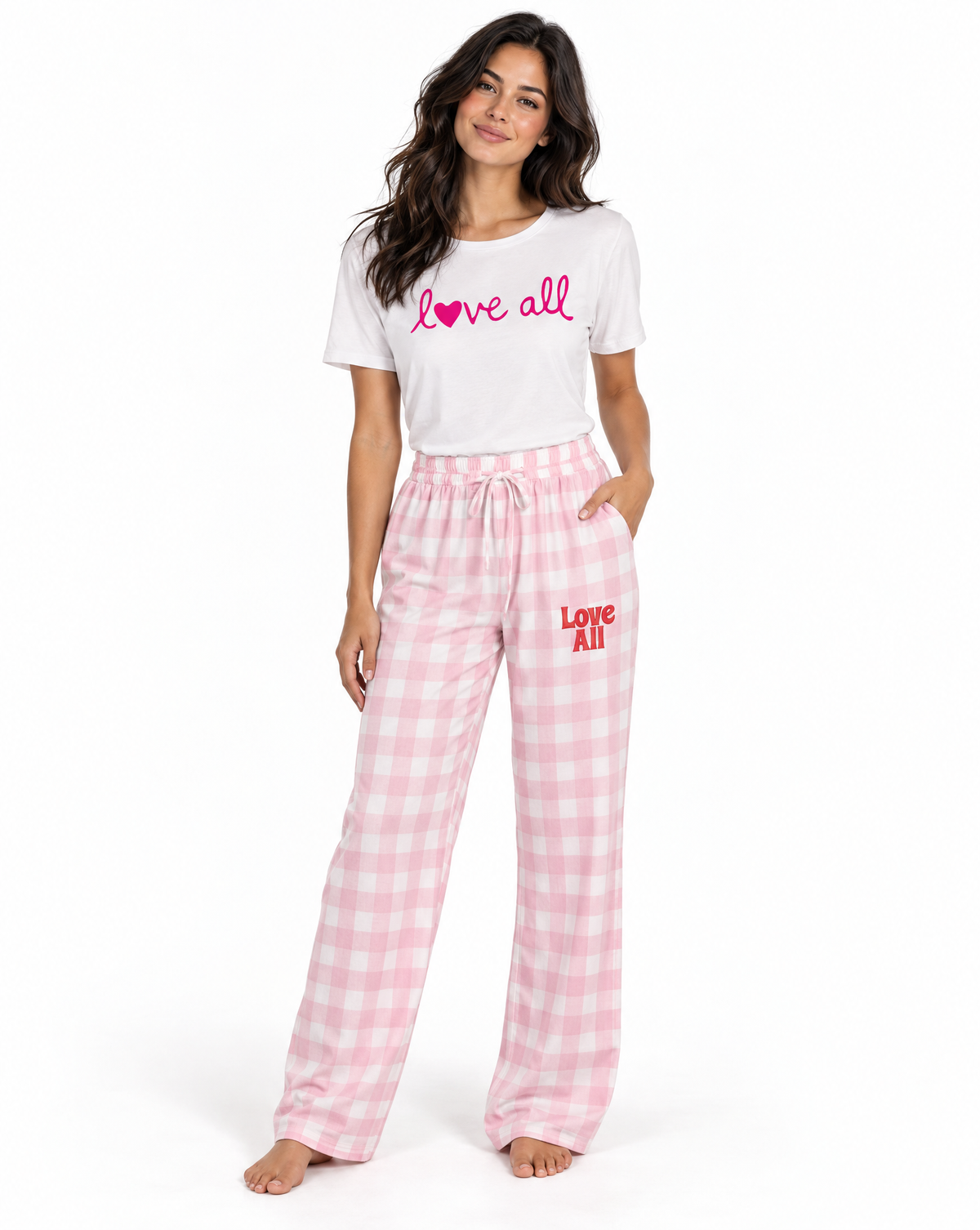 A woman modeling a matching pajama set consisting of a white short-sleeve t-shirt with pink 'love all' script text and pink-and-white gingham lounge pants with red 'Love All' text on the leg, against a plain white background.