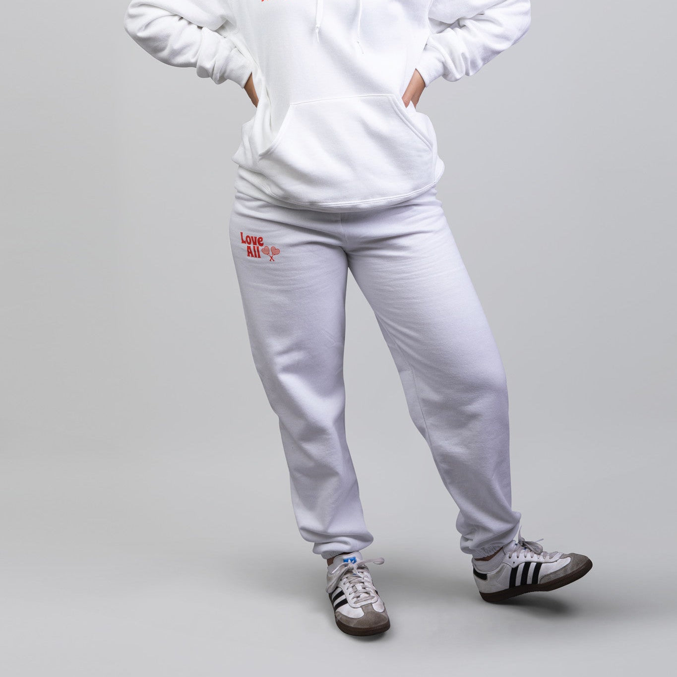Person wearing a white hoodie and pants set with visible branding on a gray background