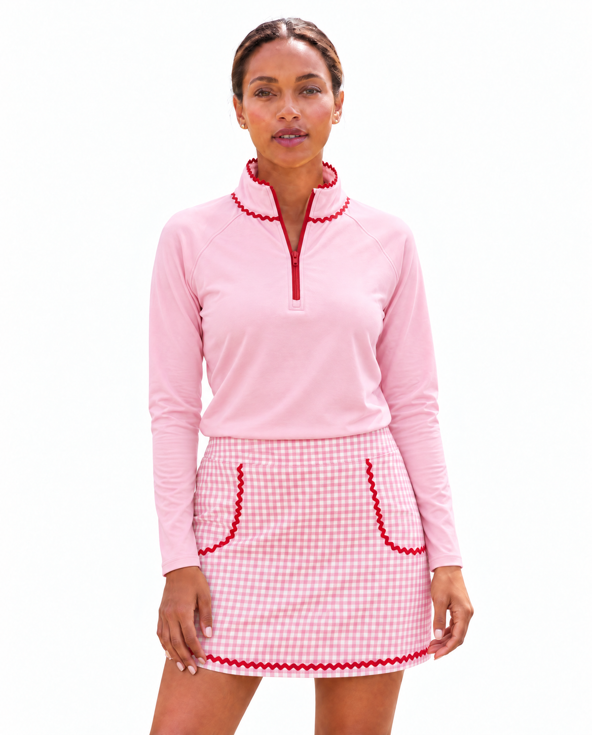 A woman modeling a pink long-sleeve quarter-zip top and a pink-and-white gingham mini skirt with red trim, set against a plain white background.