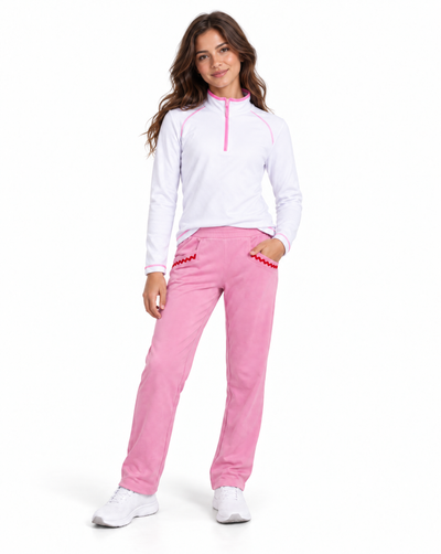 A woman modeling a white long-sleeve quarter-zip athletic top with pink trim and matching pink pants with red trim, standing against a plain white background.