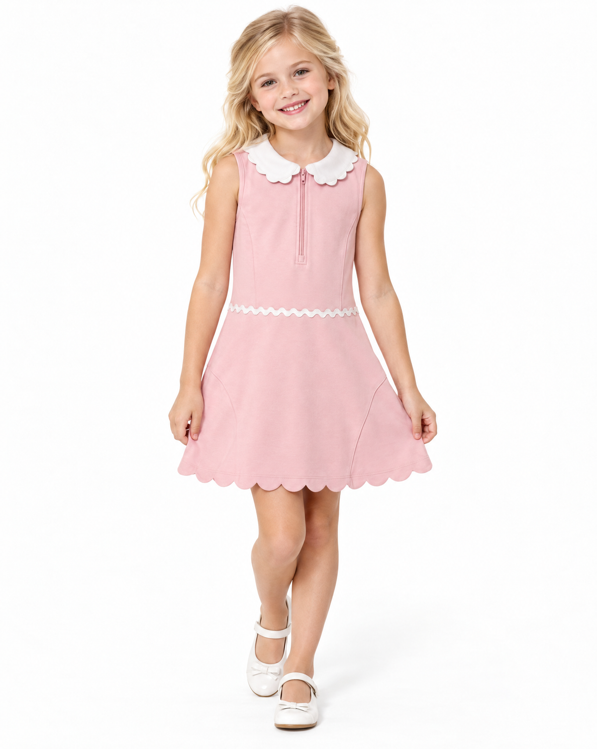 A young girl with blonde hair wearing a sleeveless pink dress with a white scalloped Peter Pan collar, white lace trim at the waist, and white Mary Jane shoes, standing against a plain white background.