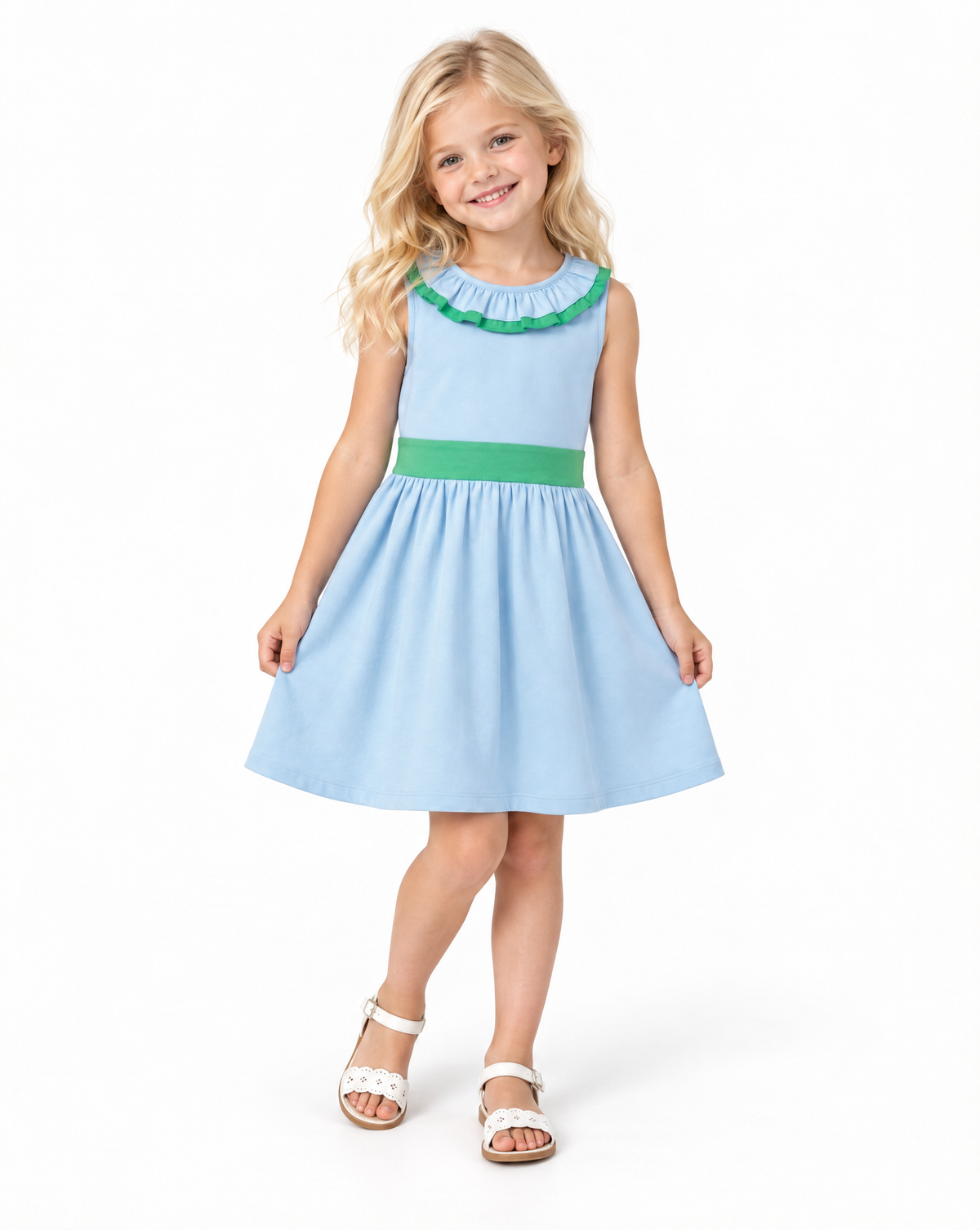 A young girl with blonde hair is wearing a light blue sleeveless dress with a green ruffled collar and a green waistband, paired with white sandals, against a plain white background.