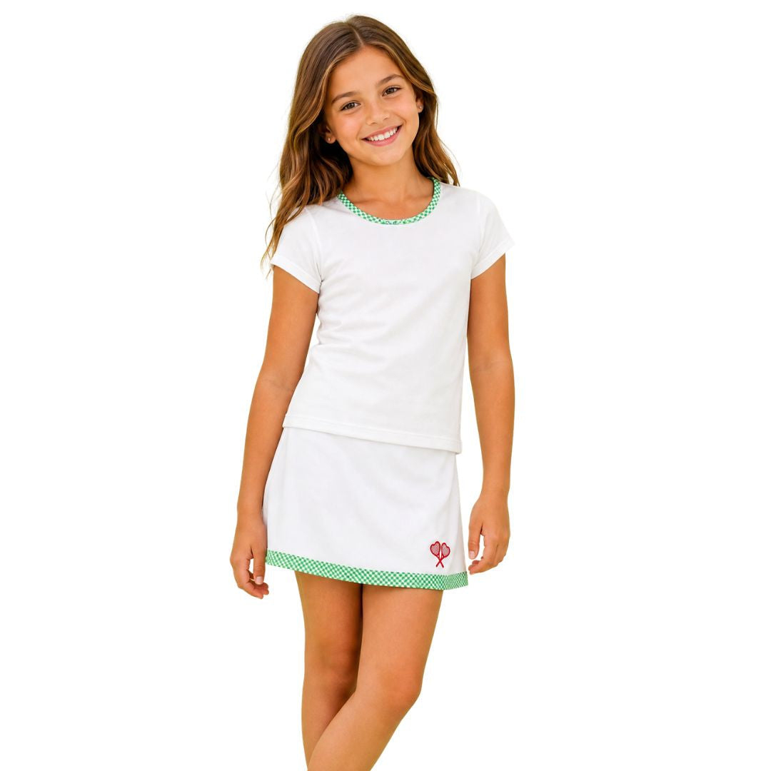 Young girl wearing a white outfit with a skirt and t-shirt with green detail on a white background