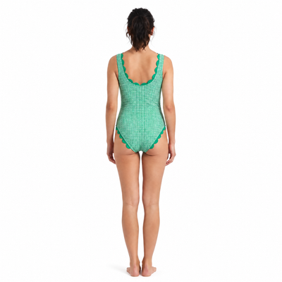 A woman viewed from the back wearing a green and white gingham one-piece swimsuit with a scalloped green trim, standing against a plain white background.