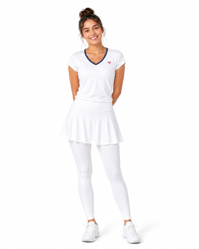 Woman wearing a white v-neck athletic short sleeve top with navy trim and white skirted leggings and sneakers on a flat white background