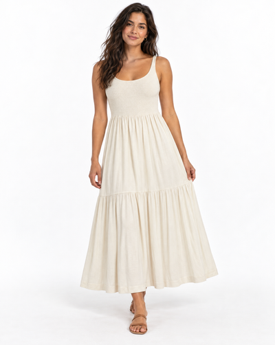 A woman modeling a sleeveless, tiered maxi dress in a warm off-white or cream color, standing against a plain white studio background.