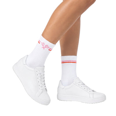 Crew socks with pink and red stripes and pink crossed heart tennis racket logo on model wearing white sneakers set against a white background