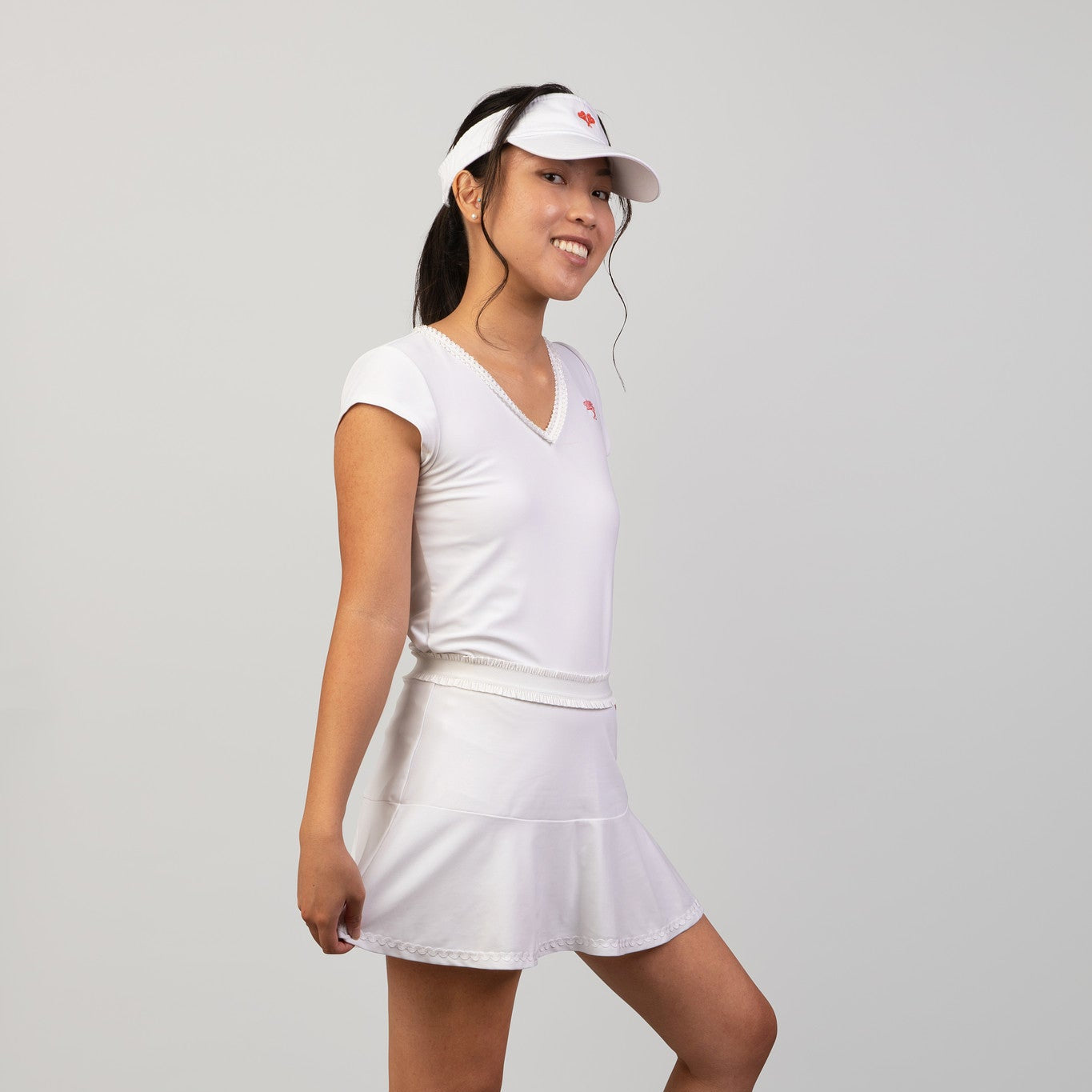 Woman in white tennis outfit with visor on a gray background