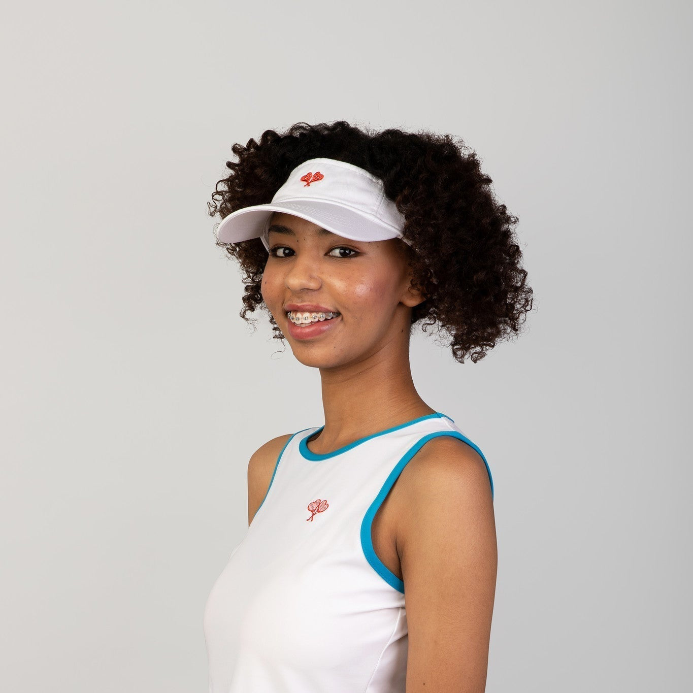 Woman wearing a white tank top and visor with a red logo on a gray background