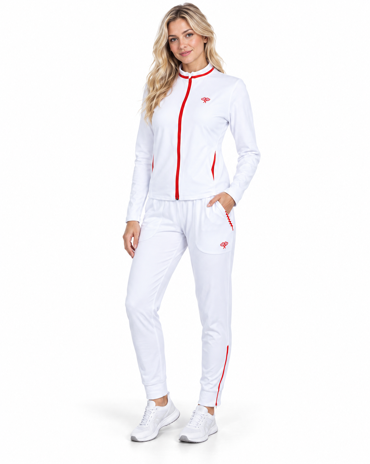 A woman modeling a white athletic tracksuit with red trim and a small red logo, consisting of a zip-up jacket and matching jogger pants, against a plain white background.