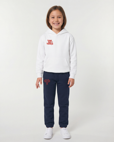 Child wearing a white hoodie and navy tracksuit with red designs on a white background