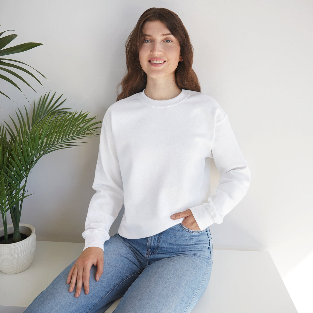 Person wearing a white sweatshirt and jeans sitting on a bench next to a fern type plant 