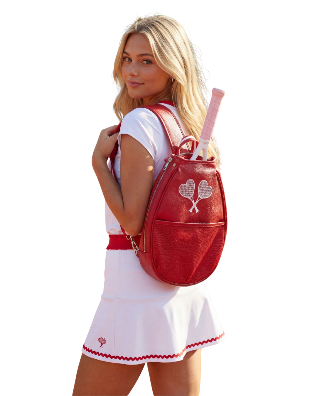 A blonde woman wearing a white tennis outfit and holding a pink tennis racket, shown from the back wearing a red leather tennis backpack with a silver heart design.
