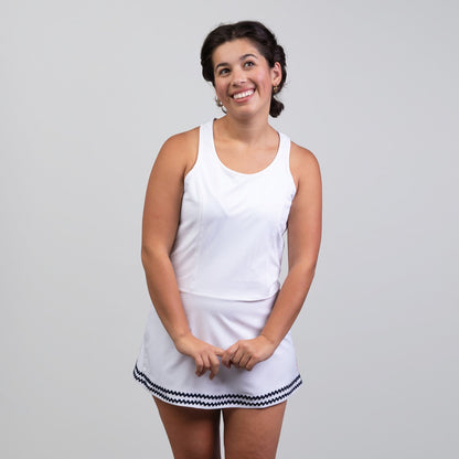 Woman wearing a white tennis dress with a skirt on a plain background