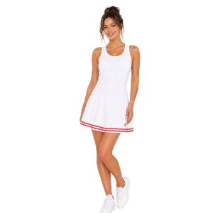 A woman modeling a white sleeveless tennis dress with red trim on the hem, paired with white sneakers, against a plain white background.