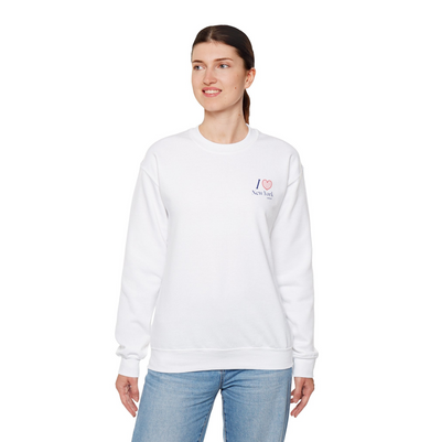 Woman wearing a white sweatshirt with a "I heart New York" graphic on the left hand side of the chest with jeans on white studio background