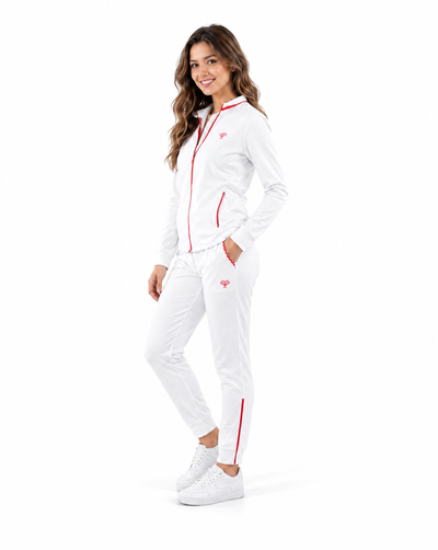 A woman modeling a white tracksuit with red trim, featuring a zip-up jacket and matching pants, against a solid white background.
