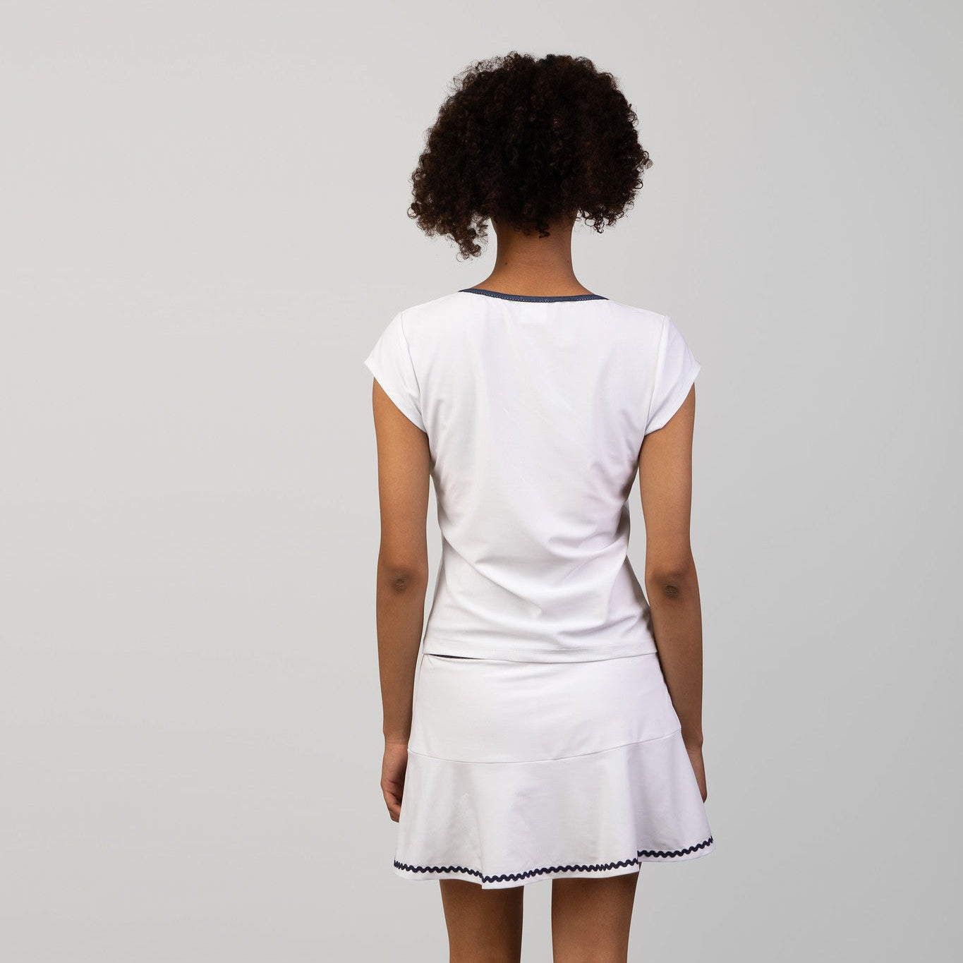Person wearing a white tennis skort and top with a skirt on a plain background