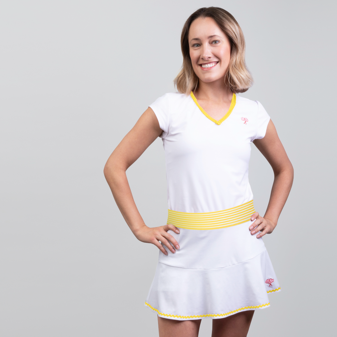 Woman wearing a white tennis dress with yellow accents on a gray background