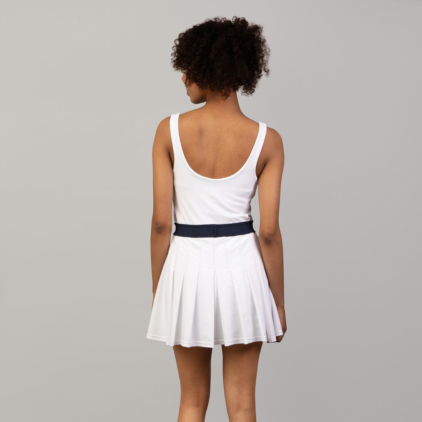 Person wearing a white sleeveless dress with a navy belt on a gray background