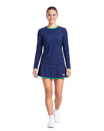 A woman wearing a navy blue long-sleeve athletic dress with a flared skirt and thin green trim, paired with white socks and white sneakers, on a plain white background.