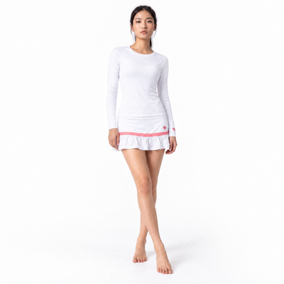 A woman modeling a white long-sleeve athletic top and skirt with a pink ruffled hem and a small red logo on the sleeve, set against a plain white studio background.