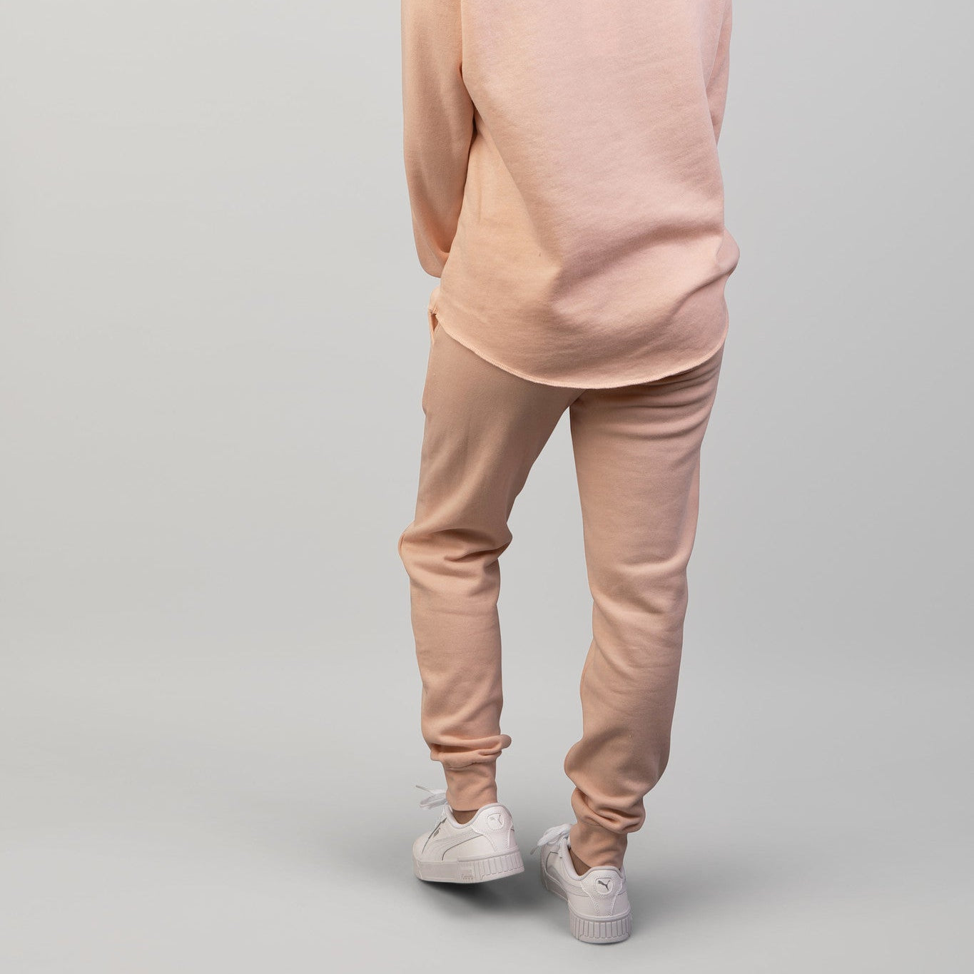 Person wearing a peach sweatshirt and pants on a gray background