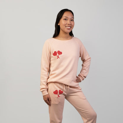 Woman wearing a peach sweatsuit set with red heart tennis racket designs on a gray background