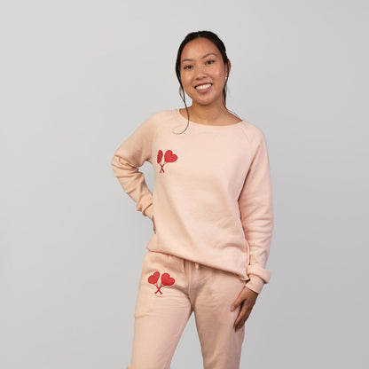 Person wearing a matching peach sweatshirt and pants set with heart designs on a gray background