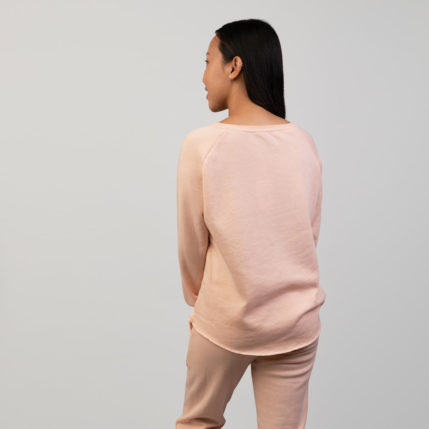 Person wearing a peach sweatshirt and pants on a gray background