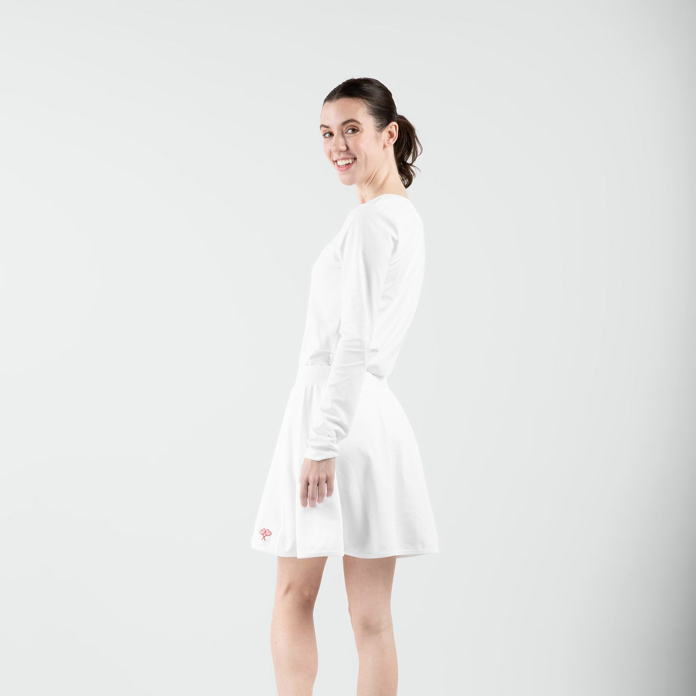 Woman wearing a white top and skort standing against a plain background