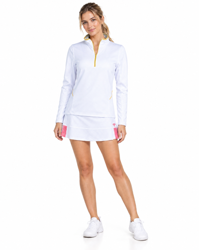 A woman modeling a white long-sleeve athletic half-zip top and matching mini skirt set with small pink and yellow accents, paired with white sneakers, against a plain white background.