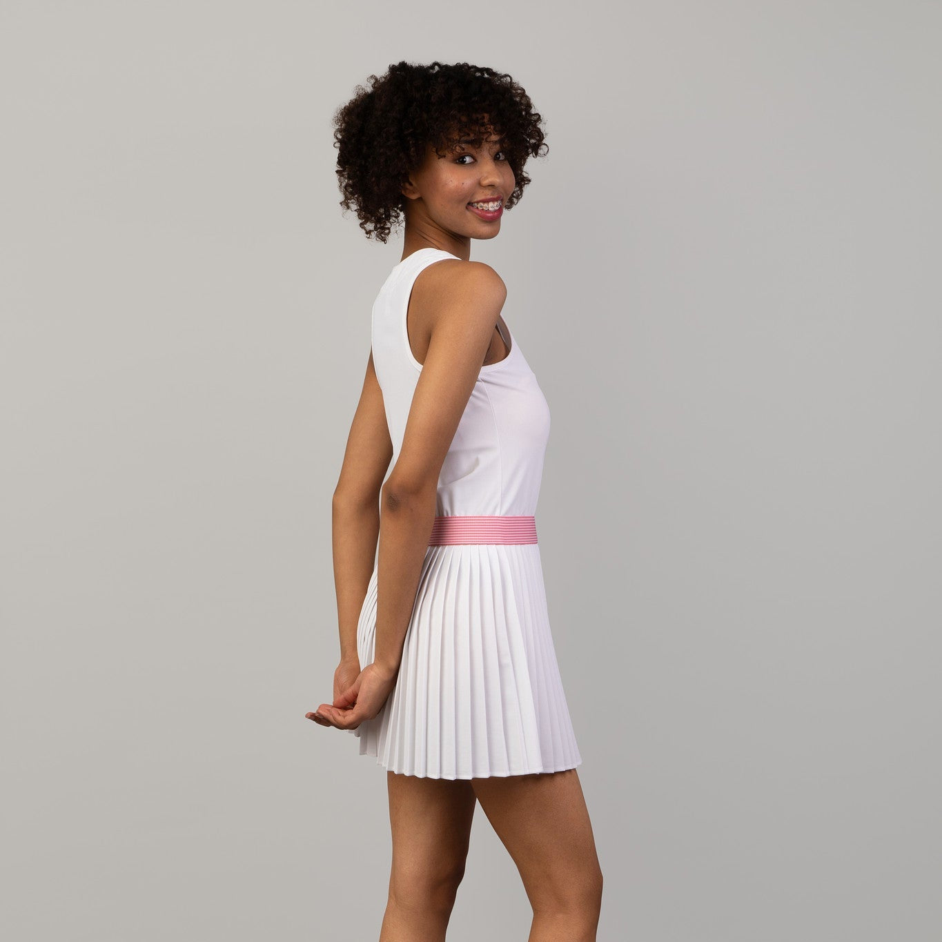 Woman wearing a white dress with a pink belt on a gray background