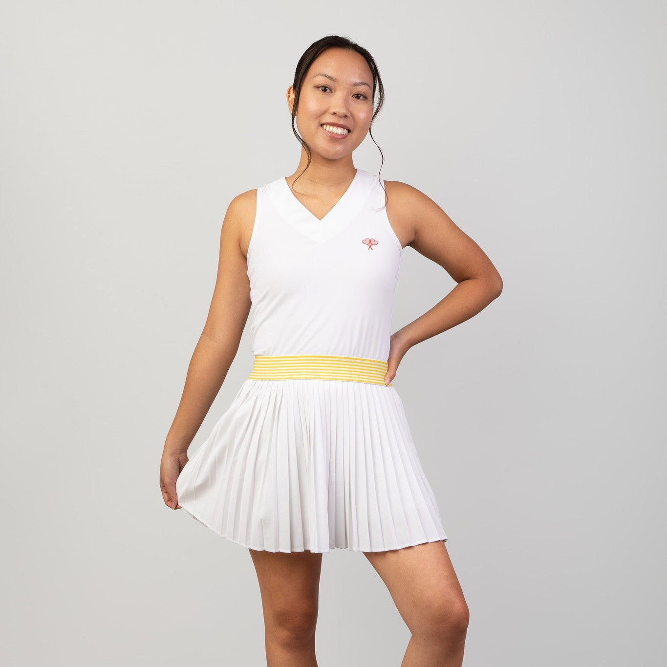 Woman wearing a white tennis dress with a yellow waistband on a gray background