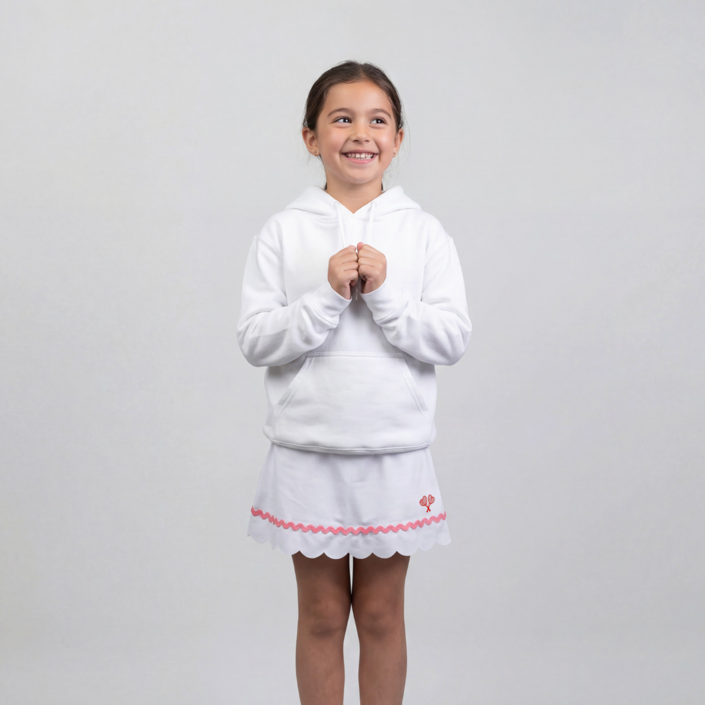 Young girl wearing a white hoodie and skirt with pink trim on a light gray background