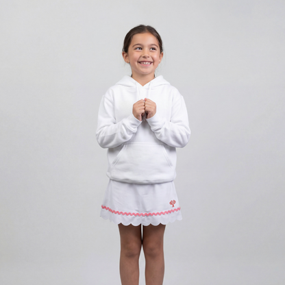 Young girl wearing a white hoodie and skirt with pink trim on a light gray background
